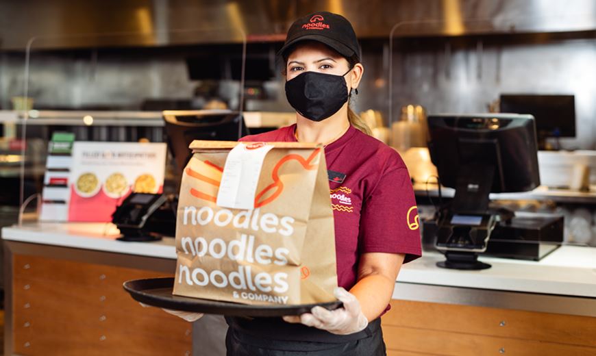 Noodles & Company franchise team member holds up a takeout order