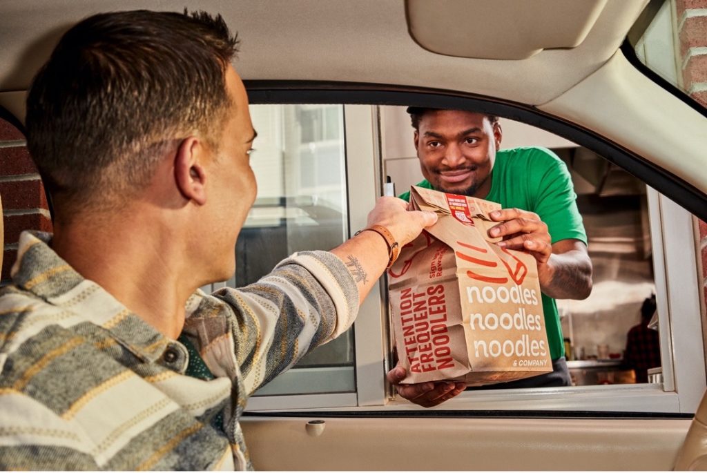 Noodles & Company employee giving a take-out order to a guest through drive-thru window